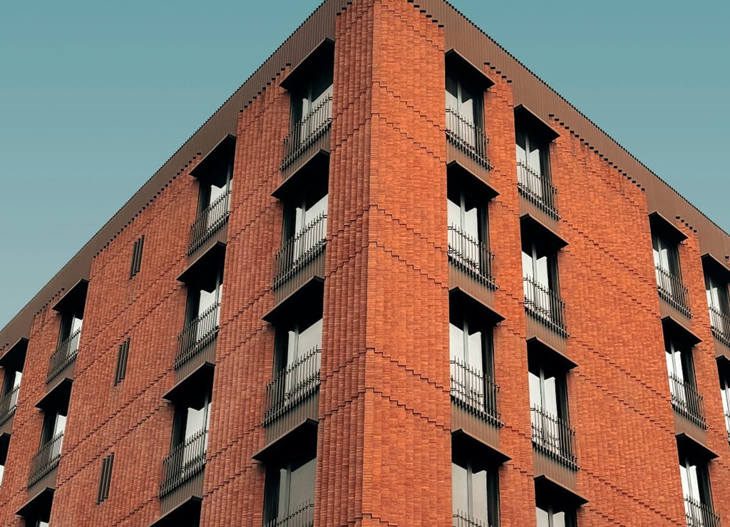 Modern red brick apartment or office building viewed from below against a clear sky.